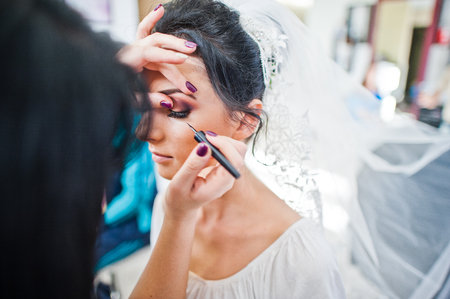 Makeup artist or beautician doing wedding makeup for a gorgeous young bride in a salon.の写真素材