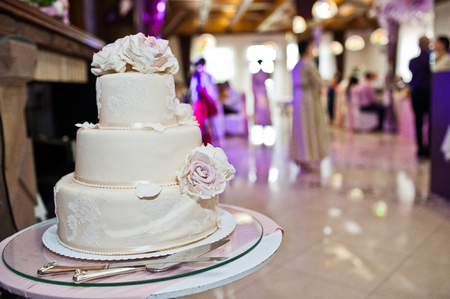 Delicious white and beige wedding cake decorated with flowers standing on the table in restaurant.の写真素材