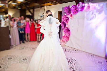 Happy wedding couple performing their first dance and kissing in restaurant in front of guests.の写真素材
