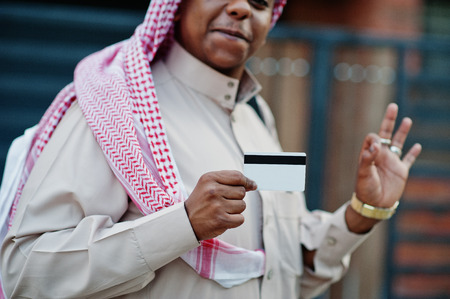Middle Eastern arab business man posed on street against modern building with black handbag and credit card at hand.の写真素材
