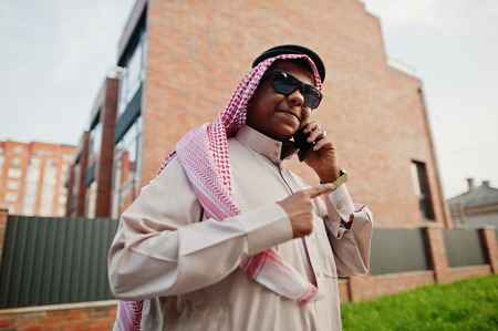 Middle Eastern arab business man posed on street against modern building with sunglasses, speaking on mobile phone.の写真素材