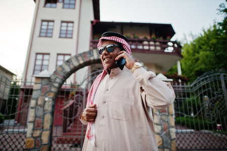 Rich Middle Eastern arab business man with sunglasses posed on street against mansion , speaking on mobile phone.の写真素材