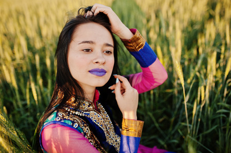 Tender indian girl in saree, with violet lips make up posed at field in sunset. Fashionable india...