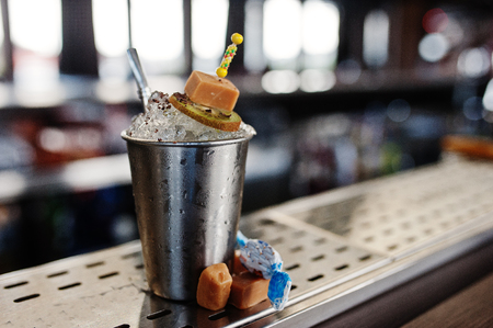 Alcoholic cocktail with sweets and candies in small silver bucket at bar table.の写真素材