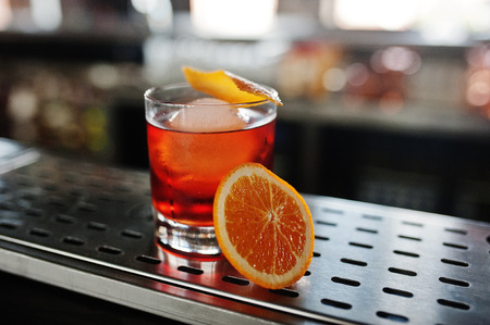 Alcoholic cocktail with ice and orange in glass on bar table.
