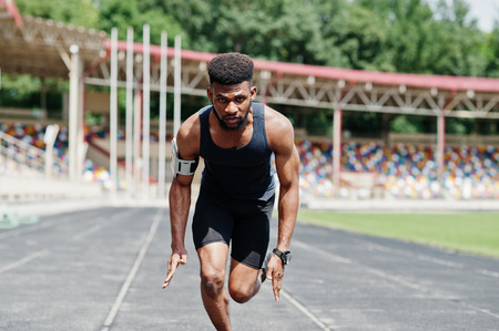 African american male athlete in sportswear racing alone down a running track at stadium.