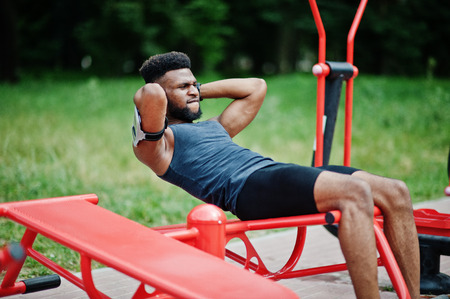 African american male athlete sport man with running sports arm case for mobile phone, doing exercises on the street workout simulators.の写真素材