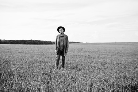 Stylish man in glasses, brown jacket and hat posed on green field.の写真素材