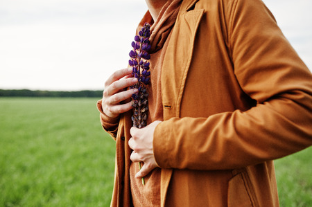 Stylish man in glasses, brown jacket and hat posed on green field.