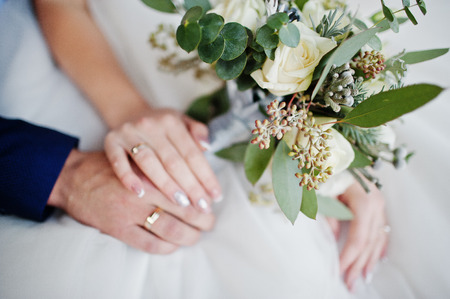 Close-up photo of groom's and bride's hands with rings and bouquet.の写真素材