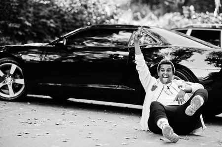 Stylish hipster arab man guy in hat posed outdoor in street against his black muscle car and shows two fingers.の写真素材