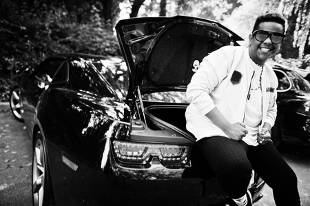 Stylish hipster arab man guy in sunglasses posed outdoor in street and sitting on the trunk his black muscle car. Rich black man.の写真素材