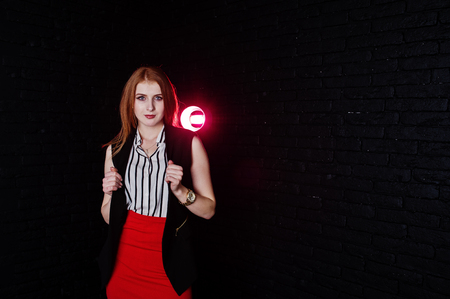 Portrait of an attractive redheaded girl in sleveless jacket, striped blouse and red trousers posing next to the brick wall.の写真素材