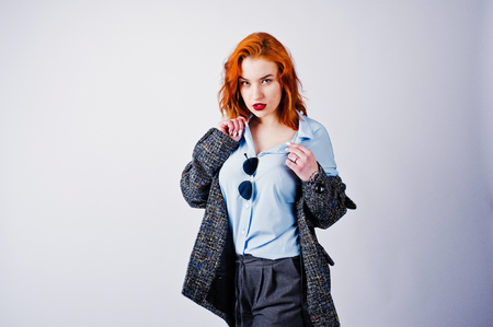 Portrait of a fantastic redheaded girl in blue shirt, grey overcoat posing with sunglasses in the studio.の写真素材