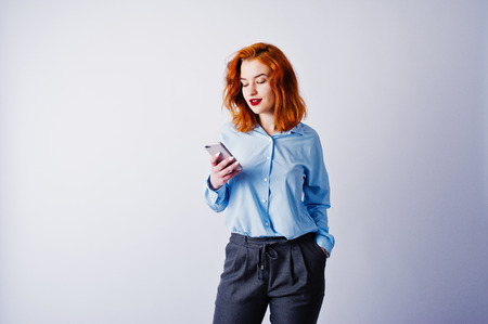 Portrait of a young redheaded businesswoman in blue shirt and trousers texting on the phone.の写真素材