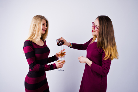 Two attractive friends in purple dresses drink sparkling wine or champagne in the studio.の写真素材