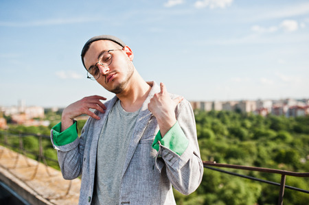 Dreamer stylish macho man in gray suit, hat and glasses posed on the roof.の写真素材