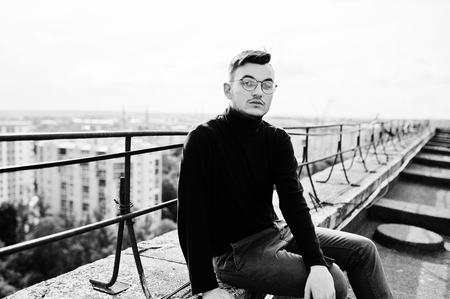 Dreamer stylish macho man in black golf and glasses posed on the roof.の写真素材