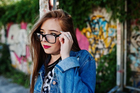 Stylish casual hipster girl in jeans wear and glasses against large graffiti wall.の写真素材