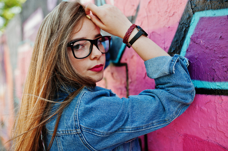 Stylish casual hipster girl in jeans wear and glasses against large graffiti wall.の写真素材