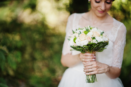 Close-up portrait of a stunning young bride holidng her bouquet in the forest.