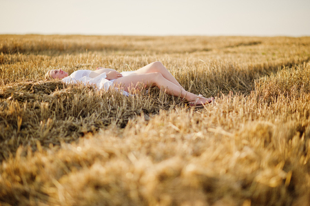 Blonde pregnant woman in wreath field at white underwear clothes on sunset. Happy moments of pregnancy.の写真素材