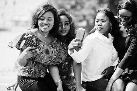 Group of four african american girls sitting outdoor and making selfie at phones.の写真素材