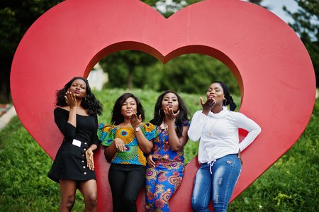 Group of four african american girls against big red heart outdoor sending air kisses.の写真素材