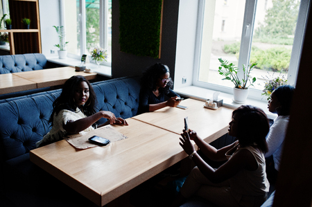Four african american girls sitting on table at cafe and looking something on mobile phone.の写真素材