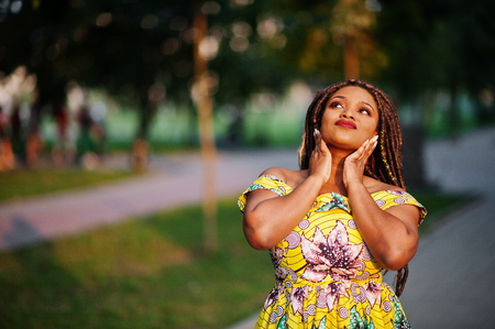 Cute small height african american girl with dreadlocks, wear at coloured yellow dress, posed at sunset.の写真素材