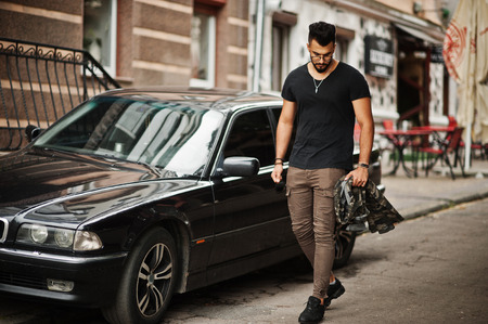 Awesome beautiful tall ararbian beard macho man in glasses and black t-shirt walking against business car.の写真素材