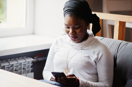 African muslim girl in black hijab sitting at cafe with mobile phone at hand.の写真素材