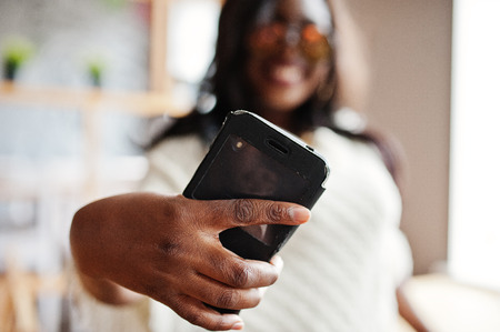 Stylish african american girl in sunglasses posed at modern cafe and making selfie on phone.の写真素材