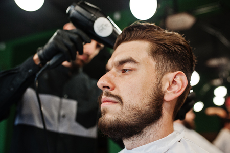 Handsome bearded man at the barbershop, barber at work, using hair dryer.の写真素材