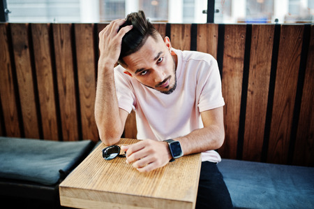 Stylish indian beard man at pink t-shirt sitting against wooden table of cafe. India model posed outdoor.の写真素材