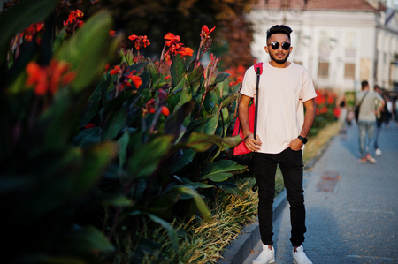 Stylish indian beard man at pink t-shirt, sunglasses and backpack. India model posed outdoor at streets of sunset city.の写真素材