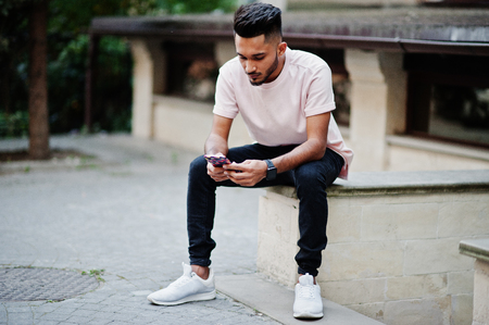 Stylish indian beard man at pink t-shirt. India model sitting with mobile phone at hands outdoor at streets of city.の写真素材
