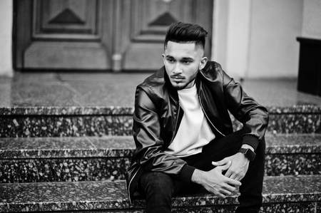 Stylish indian beard man at black leather jacket. India model posed sitting at streets of city.の写真素材