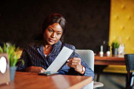 African american businesswoman sitting at table in cafe and holds a check. Black girl having rest.の写真素材