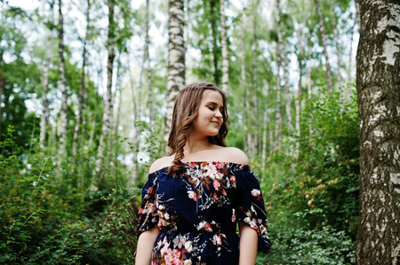 Portrait of a fabulous young girl in pretty dress with stylish curly hairstyle posing in the forest...