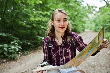 Portrait of a positive young gorgeous blonde sitting on the ground with a map in her hands in the...