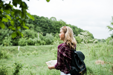 Portrait of a beautiful blond girl in tartan shirt walking with a map in the countryside.の写真素材