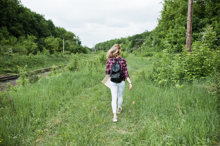 Portrait of a beautiful blond girl in tartan shirt walking with a map in the countryside.