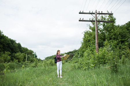 Portrait of a beautiful blond girl in tartan shirt walking with a map in the countryside.の写真素材