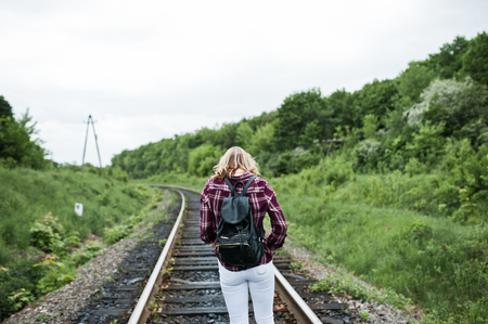 Portrait of a pretty blond girl in tartan shirt walking on the railway with map in her hands.の写真素材
