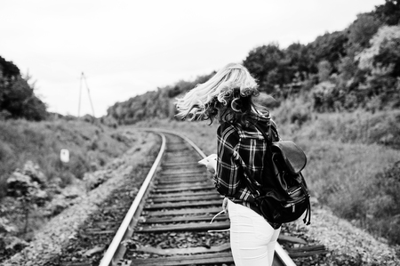 Portrait of a pretty blond girl in tartan shirt walking on the railway with map in her hands.の写真素材