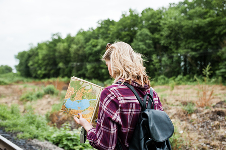 Portrait of a pretty blond girl in tartan shirt walking on the railway with map in her hands.の写真素材
