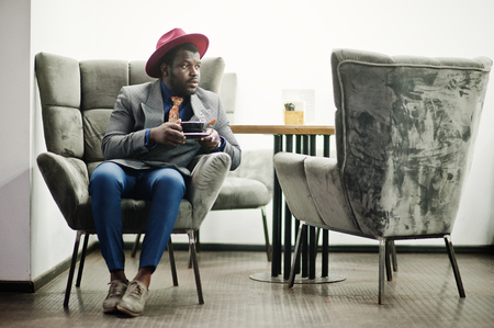 Stylish African American man model in gray jacket tie and red hat drink coffee at cafe.の写真素材