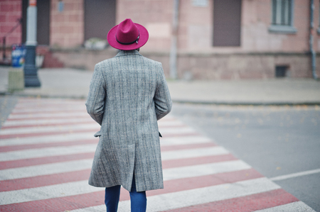 Back of walking stylish African American man model in gray coat and red hat at crosswalk.の写真素材