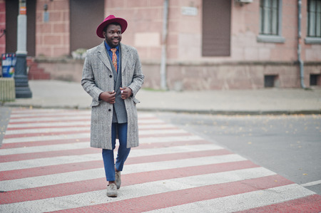Stylish African American man model in gray coat, jacket tie and red hat walking on crosswalk.の写真素材